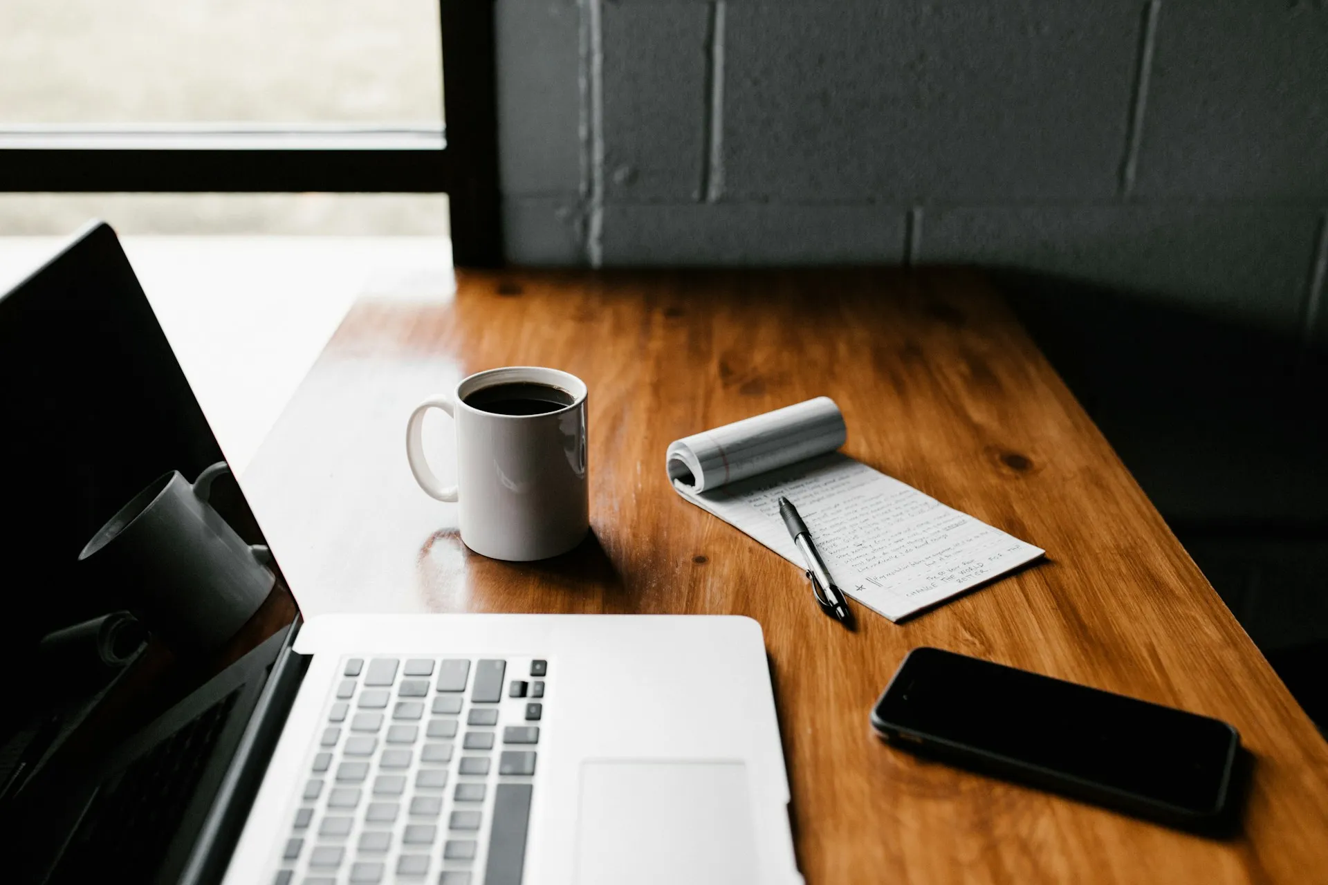 Werktafel met laptop, koffie, notitieblok en telefoon
